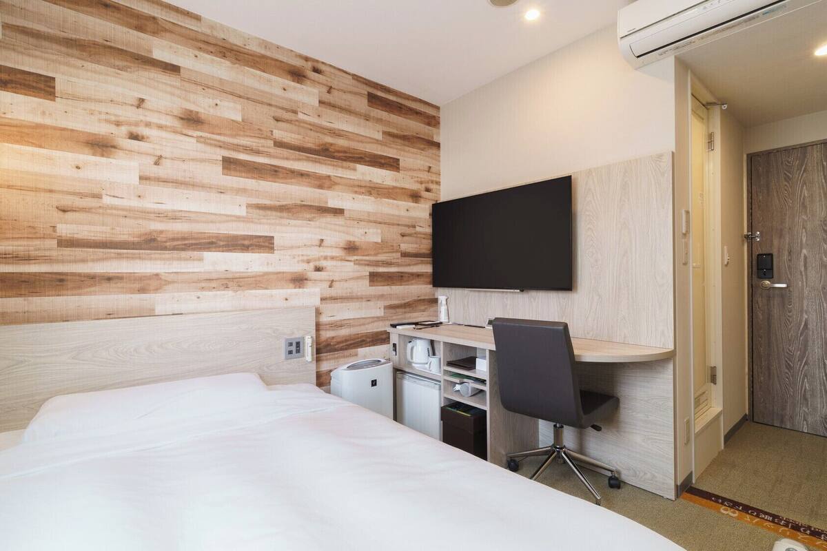 Een hotelkamer met een houten wand, een bed, een bureau met stoel, een televisie en een kitchenette.