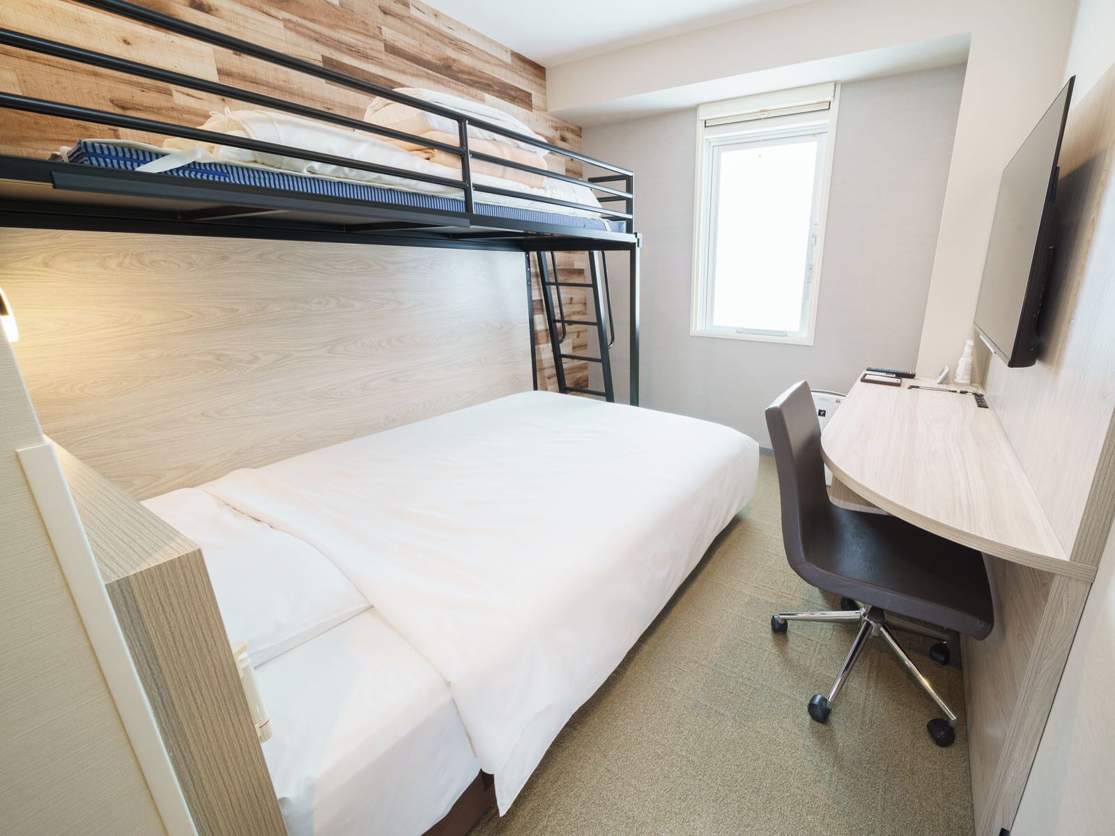 A bunk bed room with a desk and chair, a window, and a wooden wall.