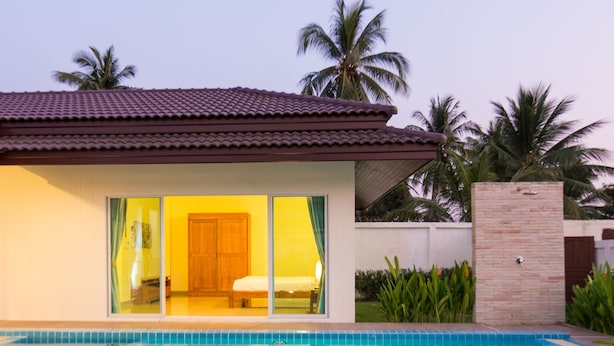 Une maison moderne dotée d’une piscine, de grandes portes vitrées donnant accès à une chambre, et d’un toit recouvert de tuiles.