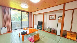 A traditional Japanese room with tatami flooring, a low wooden table, a television, and a sliding door leading to a balcony. - Kutsuroginomori Greenpia Yame (Yame)