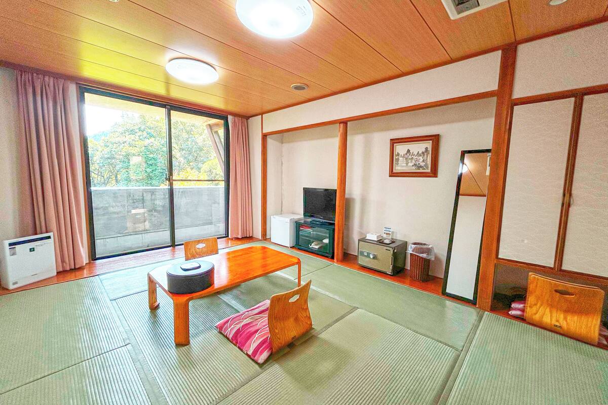 Une pièce de style japonais traditionnel, avec un sol recouvert de tatamis, une petite table en bois, un téléviseur et une porte coulissante donnant sur un balcon.
