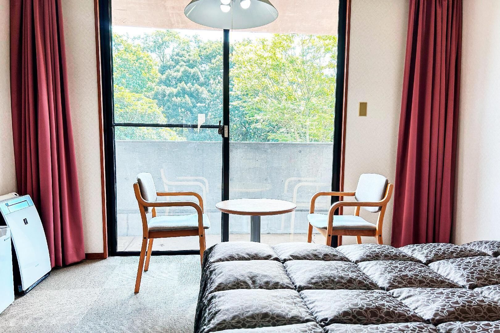 Une chambre à coucher avec un lit, deux chaises, une petite table et une fenêtre avec des rideaux.