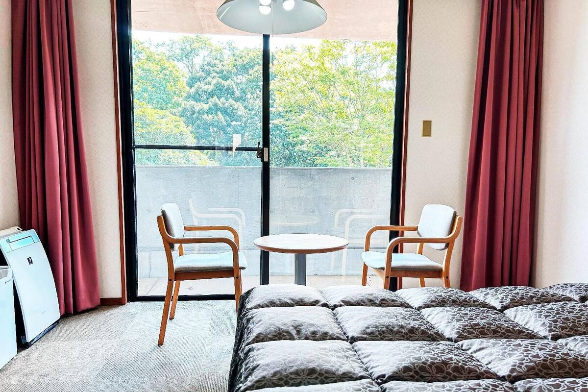 Une chambre à coucher avec un lit, deux chaises, une petite table et une fenêtre avec des rideaux.