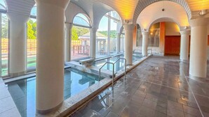 A spacious indoor swimming pool area with clear glass railings, large white columns, and arched ceilings. - Kutsuroginomori Greenpia Yame (Yame)
