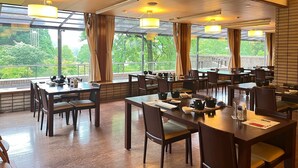 A restaurant with multiple tables and chairs, large windows with curtains, and a view of greenery outside. - Kutsuroginomori Greenpia Yame (Yame)