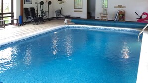 Uma piscina interior com teto de madeira, equipamentos de ginástica e um boi de flamingo flutuante.