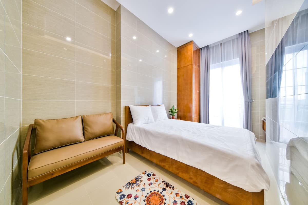 A modern bedroom with a wooden bed, a beige sofa, and a patterned rug.
