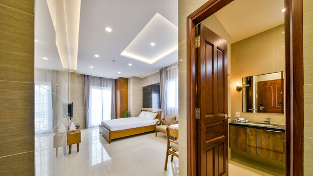 A modern hotel room with a large bed, a desk, a chair, a vanity with a mirror, and a bathroom with a sink and toilet.