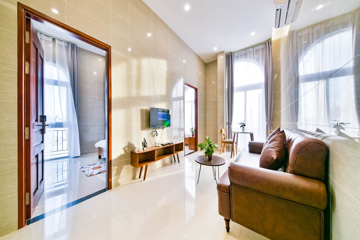 A modern hotel room with a large bed, a TV, a small table with a plant, and a sofa.