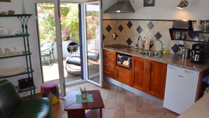 Une cuisine compacte avec des meubles en bois, un four encastré et un évier. On y trouve également un coin repas avec une table et des chaises, ainsi qu'une porte-fenêtre coulissante donnant sur une terrasse extérieure.