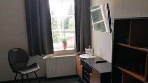 Una habitación con radiador, una silla, un escritorio con espejo y una ventana con cortinas.