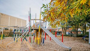 Un parque infantil con tobogán y estructuras para escalar, rodeado de arena y árboles.