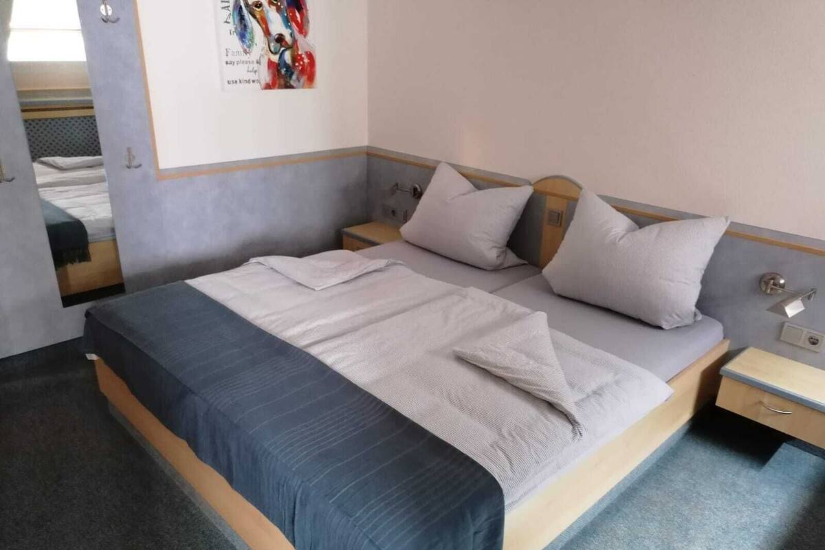 A single bed with a grey and blue bedspread, two bedside tables with lamps, and a poster on the wall.
