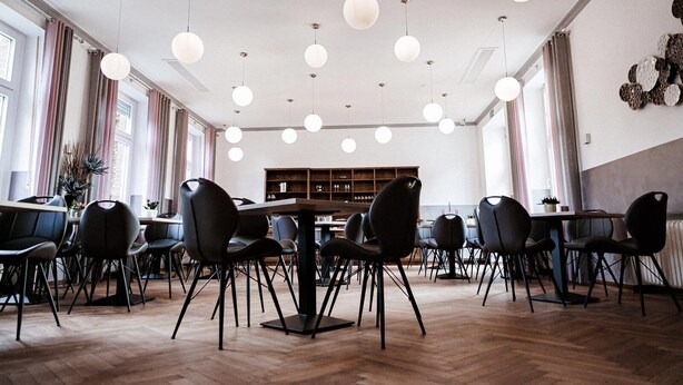 Un comedor amplio con mesas y sillas redondas, iluminación colgante y una gran estantería al fondo.