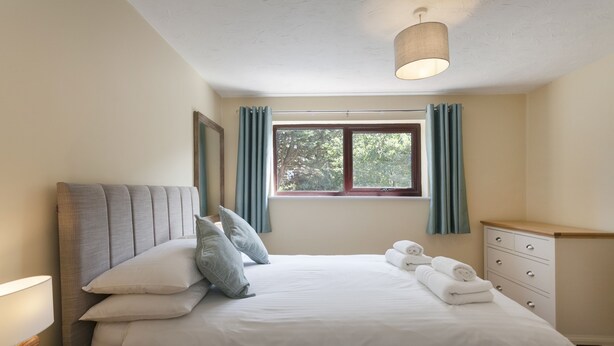 Un lit bien fait, avec des oreillers, une table de chevet avec une lampe, une commode et une fenêtre avec des rideaux.
