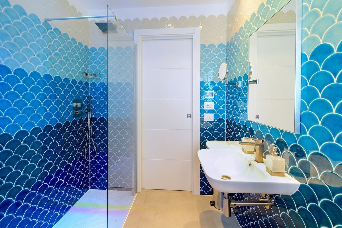 Un bagno con lavandino bianco, uno specchio e una doccia con porta in vetro.