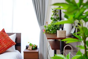 Quarto arrumado com cama, mesa de cabeceira e uma pequena planta.
