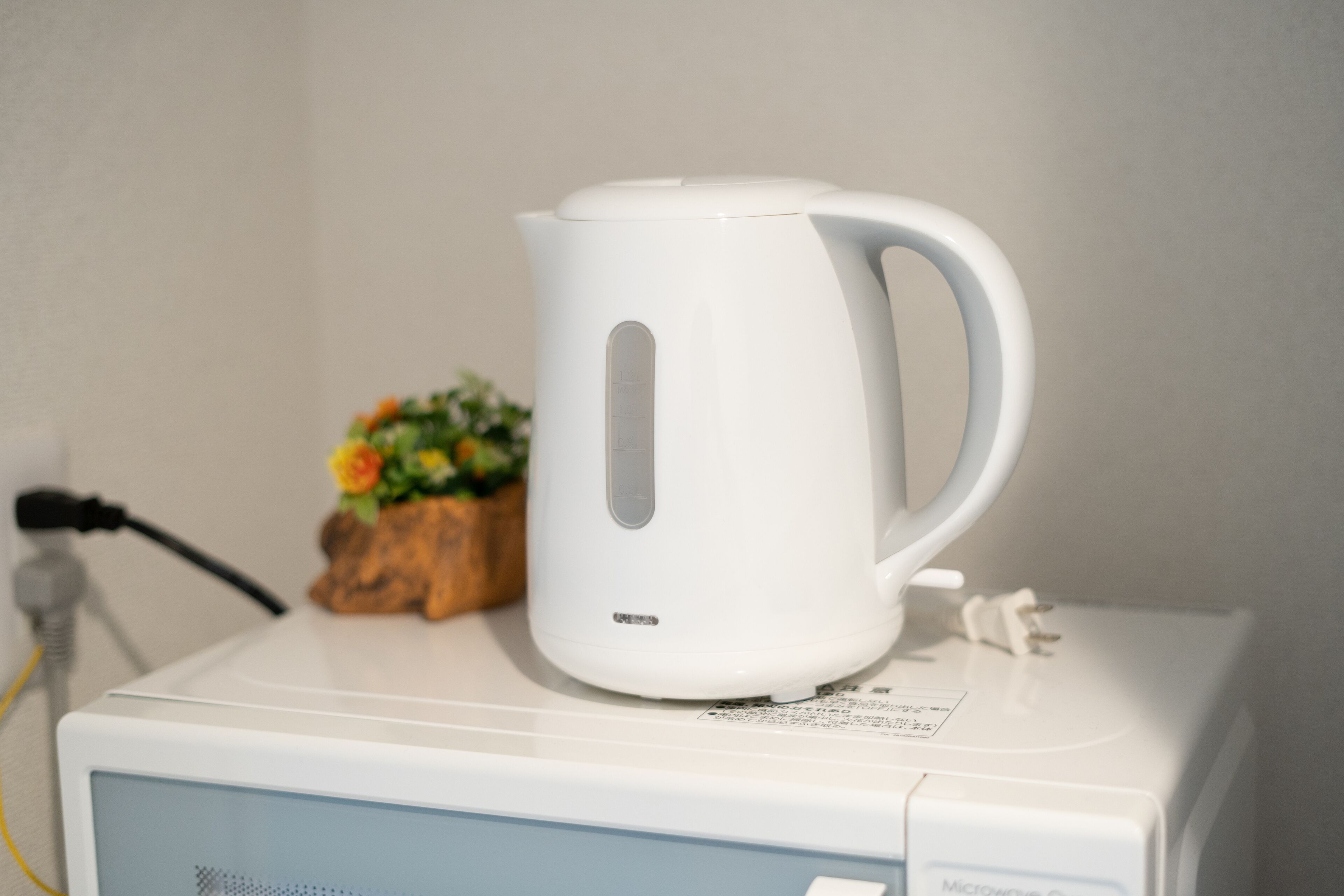 A white kettle on a microwave.