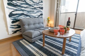 A living room with a grey sofa, a round wooden table with drinks and fruit, a striped rug, and a large abstract painting on the wall.