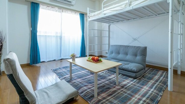 A compact room with a bunk bed, a sofa, a small table with fruit, and a plaid rug. - Liv City Shinjuku Ⅱ 504 (Tokyo)