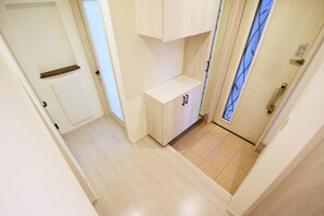 Um corredor estreito com piso de madeira clara, um pequeno banco embutido e uma porta com painéis de vidro jateado.