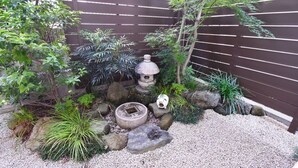 Ein kleiner Garten mit Steinlaterne, Steinen und verschiedenen Pflanzen.
