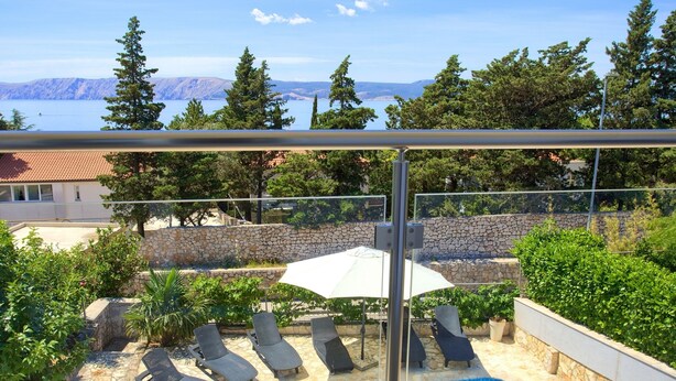 A pool area with lounge chairs and an umbrella, surrounded by stone walls and greenery, with a view of mountains and a lake. - Villa Vinodol (Kvarner - Novi Vinodolski) (Novi Vinodolski)