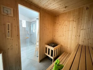 Ein Holzzaunraum mit einer Bank, einem kleinen Holzschrank und einer Glastür zu einem Duschbereich.