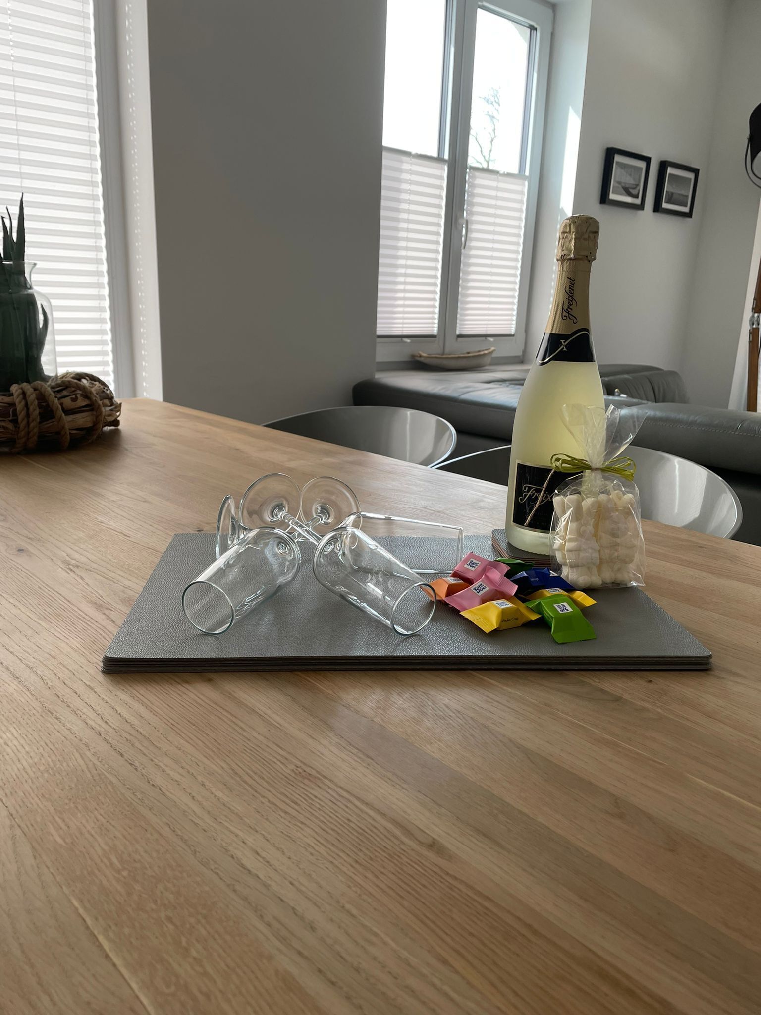 A dining table with a bottle of champagne, glasses, and colorful snacks.