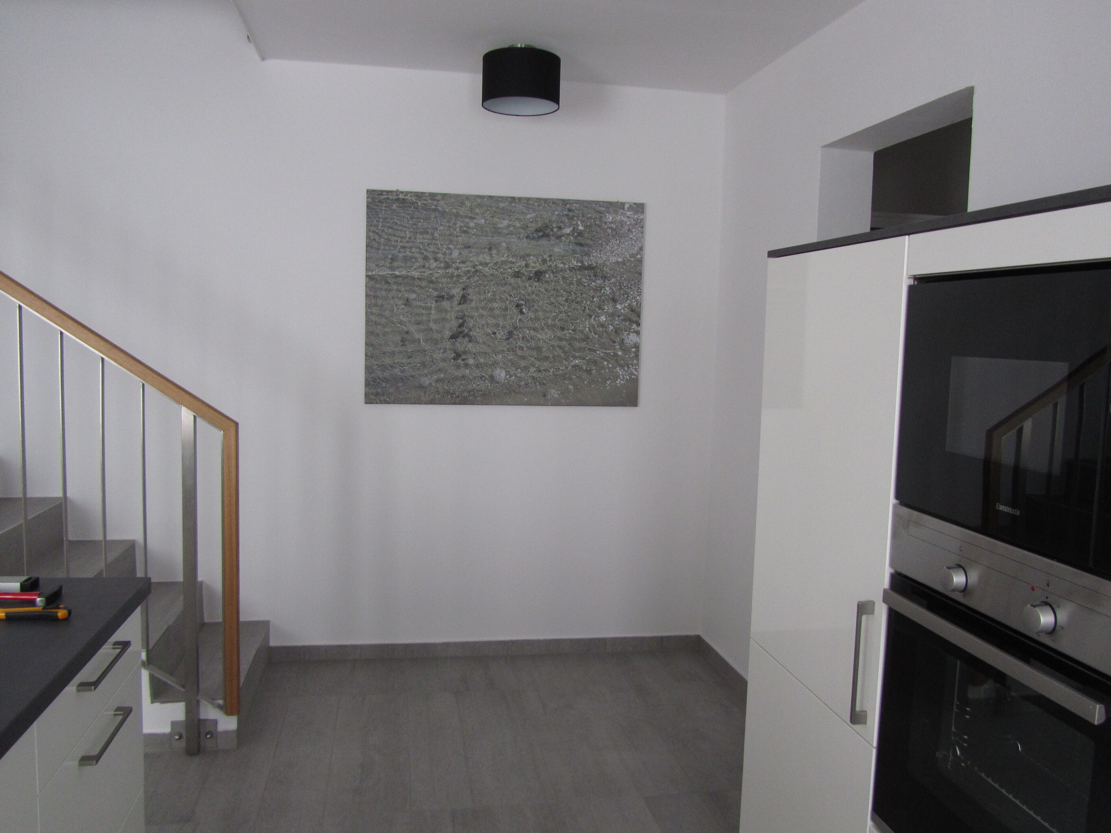 A modern kitchen with a built-in oven, a stainless steel range hood, and a wooden staircase.