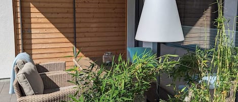 A balcony with wicker furniture, a white lamp, and potted plants.