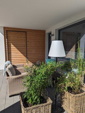 Ein Balkon mit Korbmöbeln, einer weißen Lampe und Topfpflanzen.