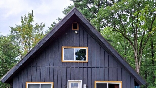 Eine dunkle Holzhütte mit einer Veranda, einer Schiebetür und einem kleinen Fenster.