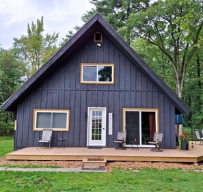 Eine dunkle Holzhütte mit einer Veranda, einer Schiebetür und einem kleinen Fenster.