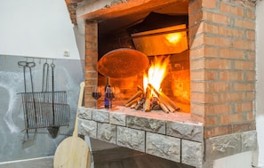 Un horno de ladrillo con fuego encendido, una rejilla metálica con utensilios y dos copas de vino sobre la encimera.