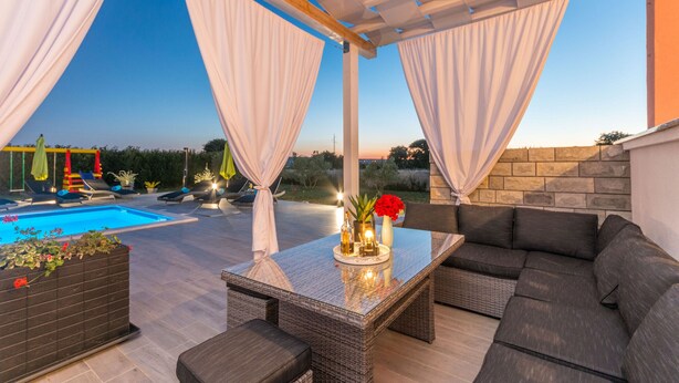 An outdoor patio with a pool, seating area, and a table with decorative items. - Villa Maris (Benkovac)
