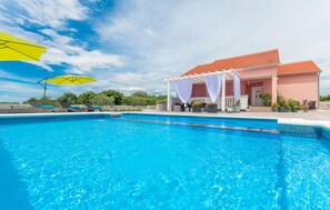 Relax by the serene pool surrounded by a shaded pergola and lush greenery.