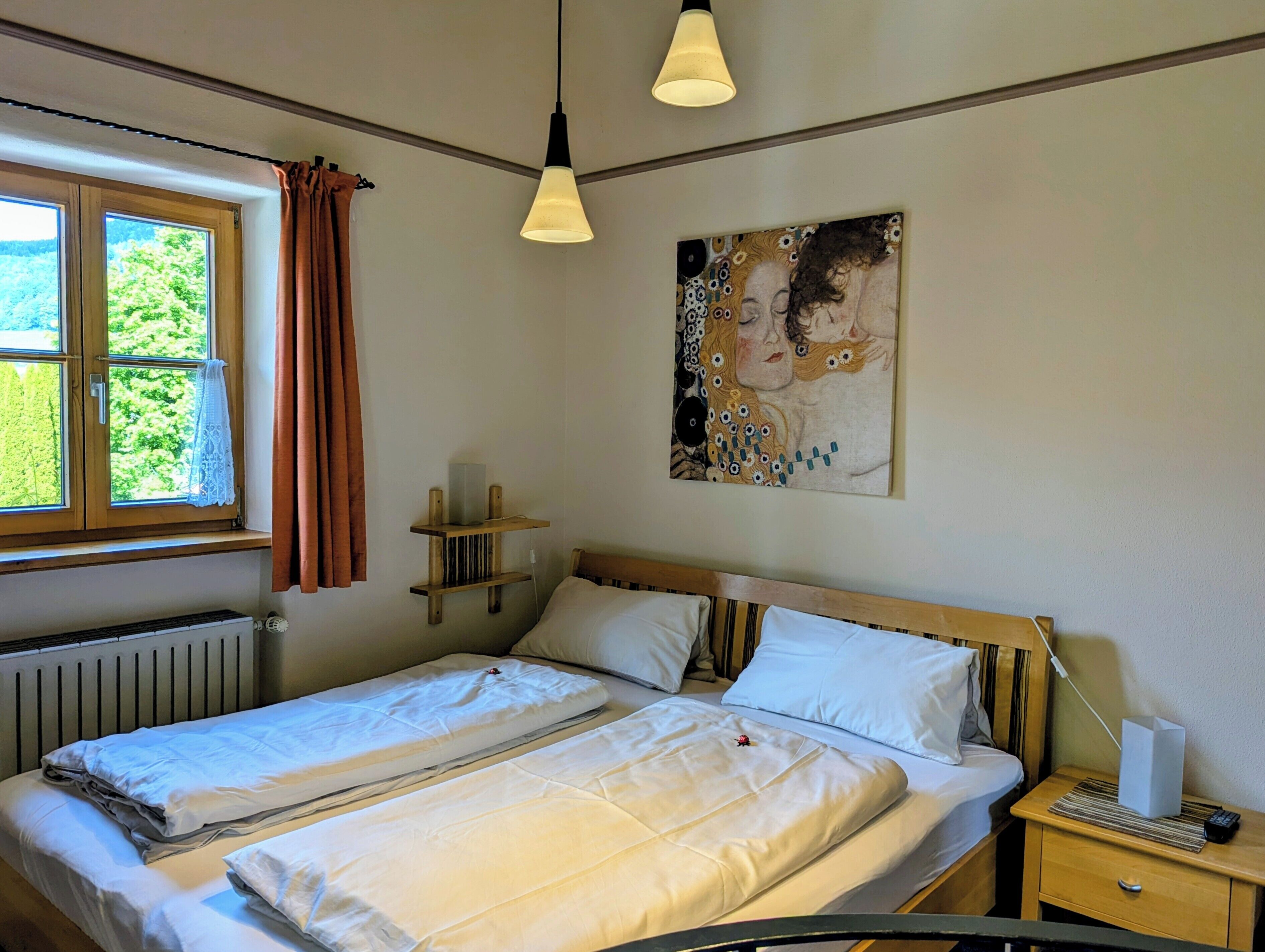 Ein Schlafzimmer mit Bett, Nachttischen, einem Heizkörper, einem Fenster mit Vorhängen und einem Bild an der Wand.