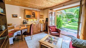 A cozy kitchen with wooden cabinets, a dining area with a table and chairs, and a large sliding glass door leading to a garden. - Ferienwohnung Rösslstube , Terr., Küche, 1 Schlaf- u. 1 Wohnz., Wlan, max 3 P (Ruhpolding)