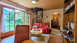 A cozy living room with a wooden ceiling, a red sofa, a wooden coffee table, and a bookshelf. - Ferienwohnung Rösslstube , Terr., Küche, 1 Schlaf- u. 1 Wohnz., Wlan, max 3 P (Ruhpolding)