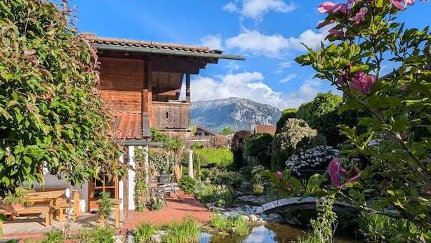A wooden house with a garden, a pond with lily pads, and a mountain in the background. - Ferienwohnung Rösslstube , Terr., Küche, 1 Schlaf- u. 1 Wohnz., Wlan, max 3 P (Ruhpolding)