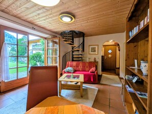 Un salon chaleureux avec un escalier en colimaçon, un canapé rouge, une bibliothèque en bois et une vue sur l’extérieur.