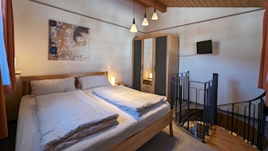 A bedroom with a wooden bed, a large wardrobe, a painting on the wall, and a TV mounted above the wardrobe. - Ferienwohnung Rösslstube , Terr., Küche, 1 Schlaf- u. 1 Wohnz., Wlan, max 3 P (Ruhpolding)