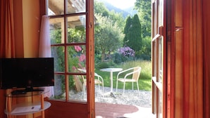 A room with a television on a glass table, a sliding glass door leading to a garden with chairs and a table outside. - Ferienwohnung Rösslstube , Terr., Küche, 1 Schlaf- u. 1 Wohnz., Wlan, max 3 P (Ruhpolding)