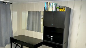 Ein Zimmer mit einem schwarzen Schreibtisch, einem Spiegel und einem Bücherregal mit Büchern und einer Obstschale.