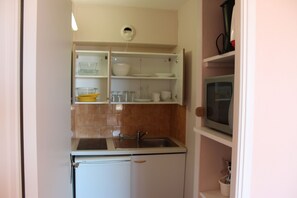 Eine kompakte Küche mit Spüle, Kühlschrank und Regalen über der Arbeitsplatte, auf denen Geschirr und Gläser stehen.