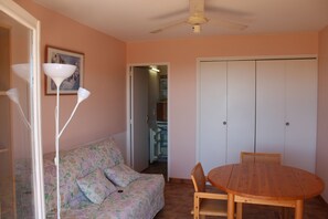 Ein Zimmer mit einem Holzesstisch, einem blumigen Sofa, einer weißen Stehlampe und einem Deckenventilator.