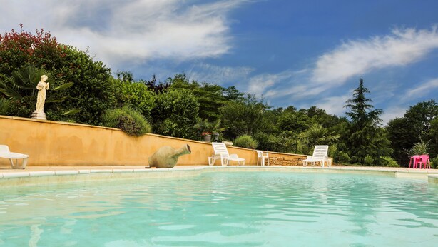 Una piscina con una estatua, sillas de descanso blancas y un muro de piedra.