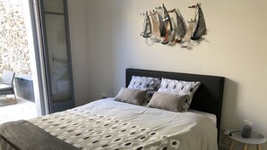 A bedroom with a bed, pillows, a bedside table, and a wall-mounted light fixture. - Etoile de Mer : T2 Avec Jardin, Accessible aux Personnes à Mobilité Réduite, (Sète)