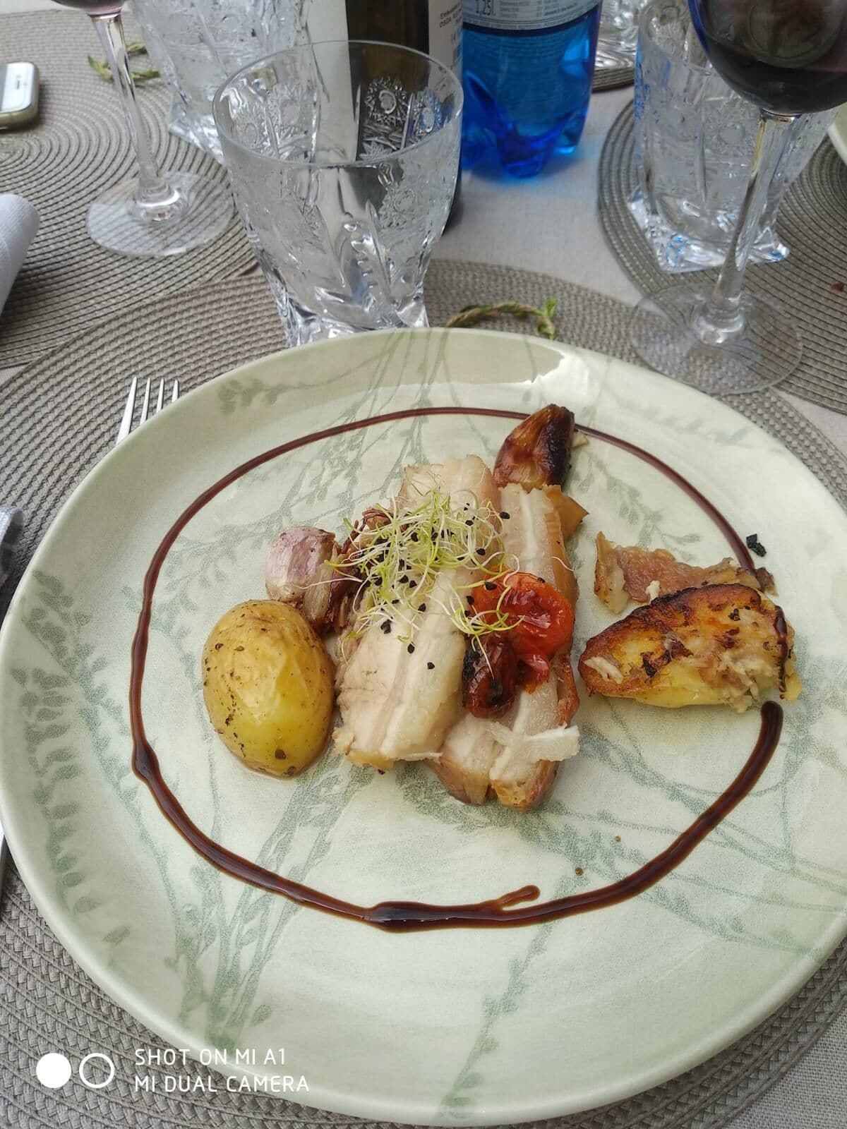 Ein Teller mit Speisen, darunter ein ganzer Fisch, eine Kartoffel und etwas Grünzeug, serviert auf einem gemusterten Teller.